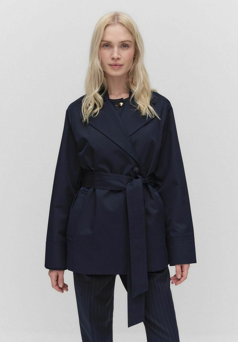 Granatowa kurtka zapinana na pasek o dopasowanym kroju, z szerokimi klapami i kieszeniami bocznymi; wykonana z gładkiego, lekkiego materiału.
