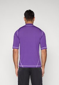 Fioletowa sportowa koszulka z krótkimi rękawami, z kontrastowym przeszyciem i dopasowanym krojem. Materiał wydaje się gładki z delikatnym połyskiem.