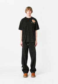 Camiseta negra de gran tamaño con un acabado texturizado y un diseño de oso en el pecho, combinada con pantalones oscuros sueltos que presentan un parche bordado.