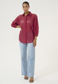 Red, sheer blouse with hexagonal pattern, button front, and long sleeves. Paired with light blue wide-leg jeans and black open-toe sandals.