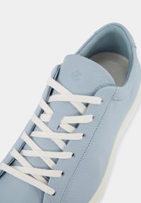 Ljusblå lädersneakers med vita snören, slät textur, rund tå och en diskret logotyp på tungan.