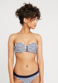 Stripete bikini i marineblått og hvitt, med bandeau topp med sentral vridd detalj og matchende lavt liv-bukser. Glatt tekstur på stoffet.