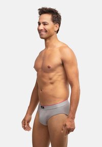 Intimo grigio con un elastico rosa, caratterizzato da un tessuto liscio e un design aderente. Modello mostrato di profilo.