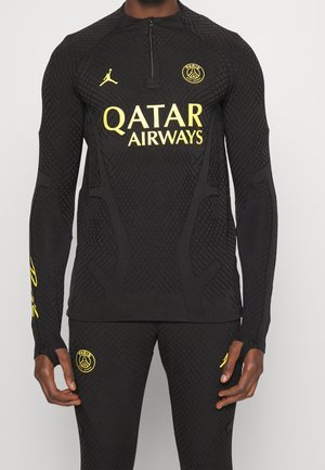 Schwarze, strukturierte Sportbekleidung mit gelben Paris Saint-Germain- und Jordan-Logos, Sponsor Qatar Airways, enganliegende lange Ärmel und sichtbare passende Hosen.