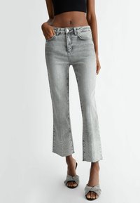 Szare dżinsy z wysokim stanem i rozszerzanym dołem, ozdobione kryształkami, z przednimi kieszeniami. W zestawie z czarnymi, fakturowanymi butami typu slip-on.