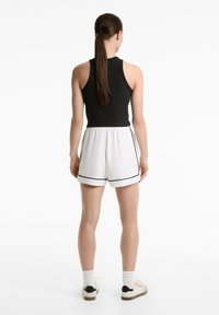 Svart ribbat linne som matchar med vita shorts med svart kant. Modell bär vita sneakers med mörka accenter och vita strumpor.