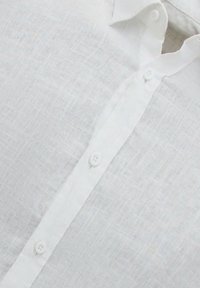 Witte linnen shirt met een puntige kraag, met een gestructureerd oppervlak en vier witte knopen langs de voorkant.