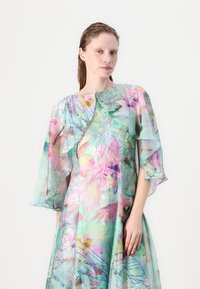 Durchsichtiges Blumenmusterkleid in Pastellfarben, mit weitem Ausschnitt und fließenden Ärmeln, aus einem geschichteten, leichten Stoff mit filigranen Mustern.