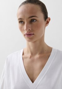 Witte katoenen v-hals top met korte mouwen, gladde textuur en een relaxte pasvorm, omkaderd door een eenvoudige halslijn en verfijnde naden.