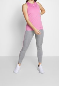 Top sportivo rosa con design a schiena scoperta abbinato a leggings grigi con una striscia laterale rosa. Scarpe da palestra bianche completano l'outfit.