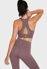 Crop top sportivo viola con design a schiena scoperta e dettaglio a chiave, abbinato a leggings a vita alta dello stesso colore, realizzati in tessuto elasticizzato.