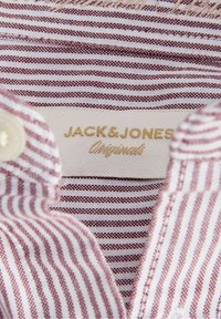 Gros plan d’un col de chemise rayé rouge et blanc montrant l’étiquette de la marque Jack & Jones Originals à l’intérieur.