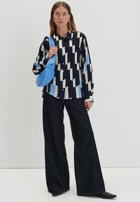 Camicia a maniche lunghe in navy, crema e blu chiaro con motivo geometrico, abbinata a jeans larghi scuri e una borsa blu chiaro.