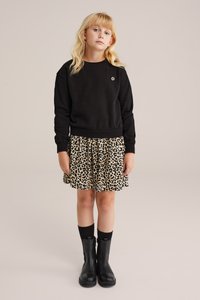 Črna sweatshirt z majhnim emblemom, v kombinaciji s bež krilom z leopardjim vzorcem. Črne škornje do kolen dopolnjujejo obleko.