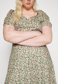 Vestido floral em tecido verde com mangas curtas e volumosas, apresentando um decote em forma de U e padrões de flores em rosa, branco e roxo por toda a peça.