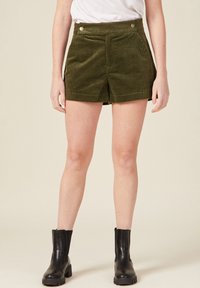 Olivgrüne Cordshorts mit hoher Taille, zwei Fronttaschen, dekorativen Knöpfen und einem Saum, der bis zur Mitte des Oberschenkels reicht.