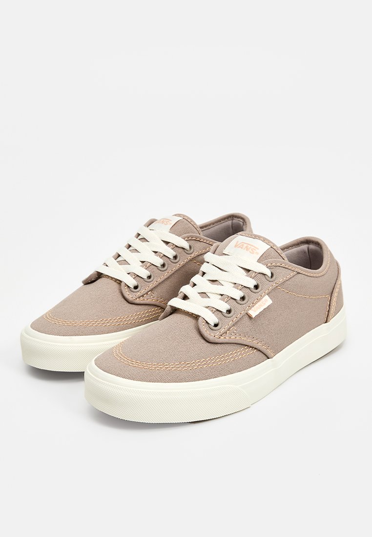 Zapatillas de lona beige con suelas de goma blancas, diseño de punta redonda, cordones blancos y un mínimo detalle de logo en el lado.