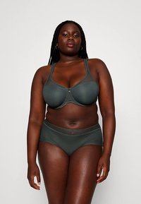 Soutien verde escuro e cuecas a condizer, apresentando um design em rede texturada e um pequeno detalhe decorativo no centro do soutien.