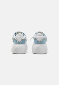 Sneakers in tela azzurro chiaro con suola bianca a coste, presenti lacci decorativi e logo sul retro. Texture liscia con design minimalista.