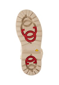 Semelle d'une botte beige avec des accents rouges, un motif de semelle texturé, des éléments en métal circulaires et des détails de marque imprimés.