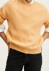 Lichtoranje geribbelde trui met korte mouwen, ronde hals en een losse fit, gecombineerd met zwarte denim broek.