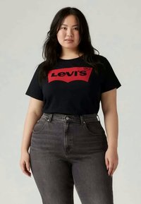 Black cotton t-shirt with red Levi's logo, paired with high-waisted dark denim jeans. Simple design, short sleeves, relaxed fit.