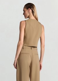Bauchfreies, ärmelloses Oberteil aus hellbraunem Stoff, kombiniert mit hoch taillierten Hosen, die Gesäßtaschen und ein schmales Paspeldetail aufweisen.