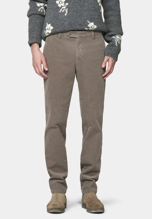 Person wearing taupe corduroy pants, brown suede boots, and a gray sweater with white floral patterns, standing with hands relaxed by sides.
