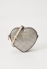 Hjerteformet metallic sølv skulderveske med beige justerbar stropp og preget GUESS-logo mønster.