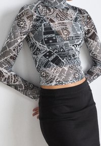 Nainen, jolla on päällä pitkähihaisen crop topin, jossa on mustavalkoinen sarjakuvaparatiisi ja kukkaprintti, yhdistettynä korkeavyötäröiseen mustaan hameeseen.