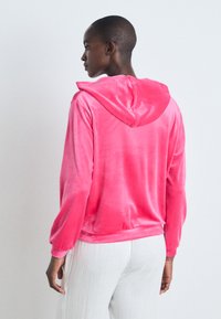 Hoodie rosa de veludo com mangas longas e capuz ajustável com cordão, textura suave, corte relaxado e punhos canelados.