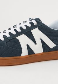 Tengerészeti bársonybőr sneaker, feltűnő fehér geometriai mintázattal, fehér fűzőkkel és textúrált barna gumitalppal.