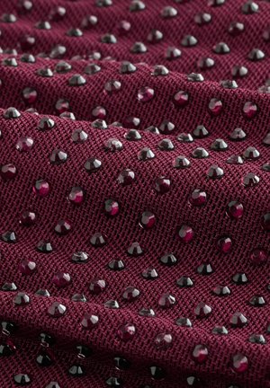 Bordó szövet texturált szövési mintázattal, fényes fekete és mélyvörös strasszokkal díszítve, amelyek szórtan helyezkednek el a felületen.