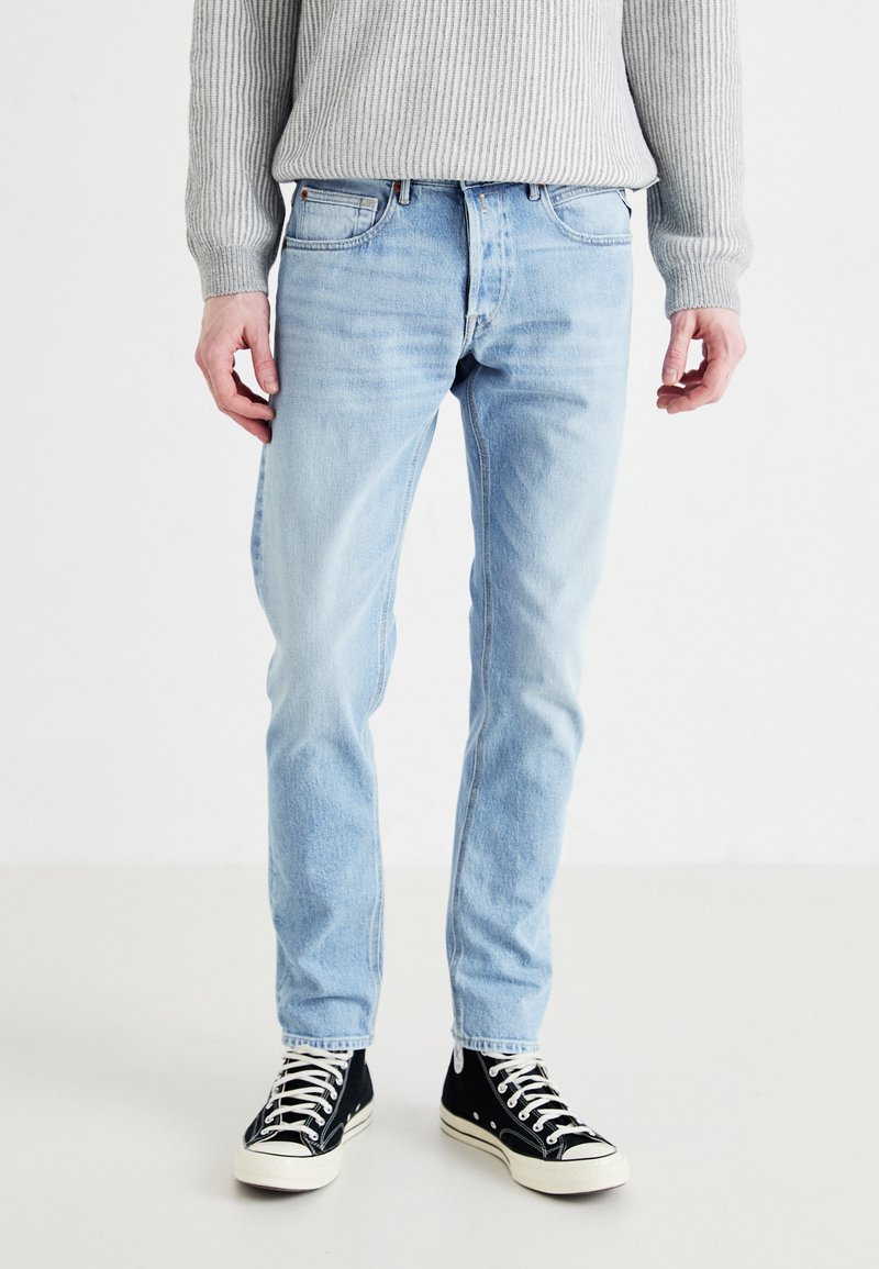 Jeans de mezclilla azul claro con corte recto, que cuentan con cinco bolsillos y una textura desgastada. Combinados con zapatillas negras de caña alta.