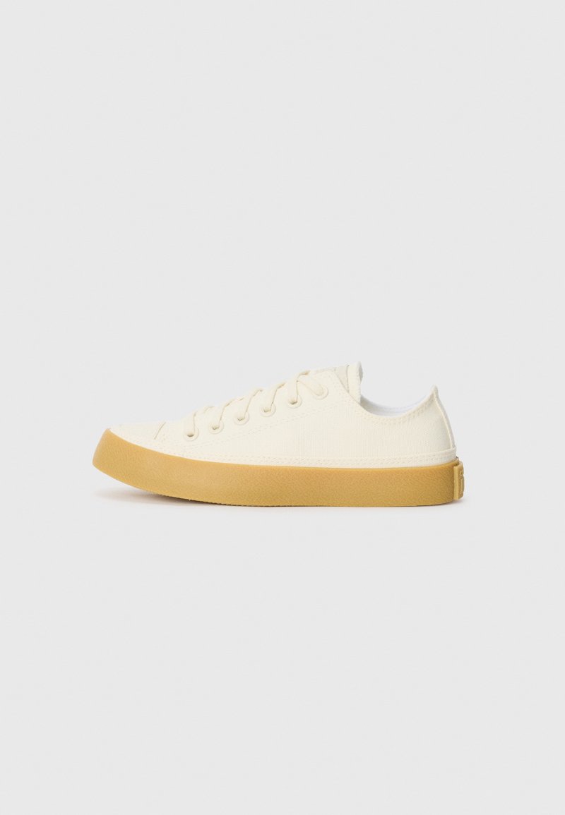 Canvas sneakers in off-white with a round toe, featuring beige rubber soles and five eyelets for laces, textured finish on the upper.