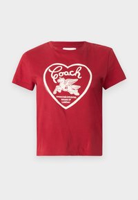 Camiseta de algodón roja con un gráfico de un corazón blanco que incluye "Coach", un caballo volador corriendo, y el texto "La Casa Original de Cuero de América".