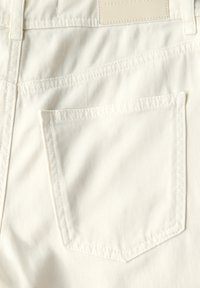 Bílá bavlněná denimová tkanina s zadní kapsou v obdélníkovém tvaru, s prošitím a koženou nálepkou nahoře.