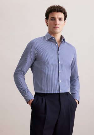 Gestreiftes Hemd in Marineblau und Weiß, mit Button-Down-Kragen, langen Ärmeln und taillierter Passform, kombiniert mit dunklen Hosen.