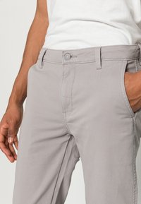 Gray cotton pants with a smooth texture, button closure, and side pockets. Features a tailored fit and simple design.