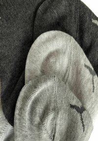Drei Paar Socken der Marke Puma in hellgrau, mittelgrau und dunkelgrau, übereinander gestapelt auf einem weißen Hintergrund.