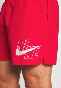 Κόκκινα αθλητικά σορτς από ελαφρύ υλικό με λευκό λογότυπο Nike και σβούρα, καθαρό σχέδιο και πλαϊνή τσέπη.