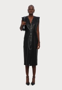 Rochie din piele neagră cu o siluetă ajustată, decolteu adânc în V și design fără mâneci. Prezintă o cusătură frontală și o lungime până la genunchi.