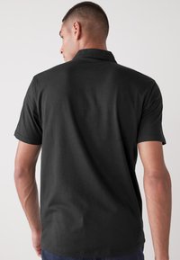 Camisa polo negra de manga corta, con cuello y dobladillo recto. La tela parece suave y ligera, sin patrones visibles.