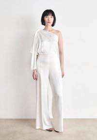 White one-shoulder jumpsuit with loose fit; satin texture; wide, flowing legs; features a draped sleeve accent.
