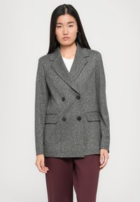 Veste grise à double boutonnage en tissu texturé, boutons noirs et deux poches avant. Associée à un pantalon bordeaux.