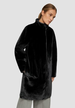 Manteau en fausse fourrure noire avec un grand col, fermeture éclair sur le devant et poches latérales ; texture douce et design mi-long.