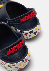 Granatowe klapki z białą podstawą z kolorowymi wzorami Myszki Miki. Czerwony napis "MICKEY" na pasku. Wykonane z trwałego, lekkiego materiału.
