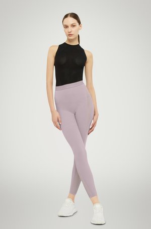 Top nero senza maniche abbinato a leggings viola chiaro con vita testurizzata e dettagli sui lati. Modello che indossa scarpe da ginnastica bianche.