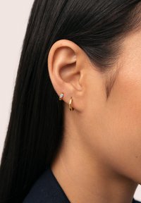 Pendiente de aro dorado y pequeño cuff para la oreja con acento azul. El aro es liso y circular, mientras que el cuff es delgado y cuenta con una piedra preciosa.