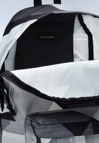 Binnenkant van een zwarte en witte rugzak met geometrisch patroon, voorzien van een ritszak en een soepele voering van stof met grijze accenten.